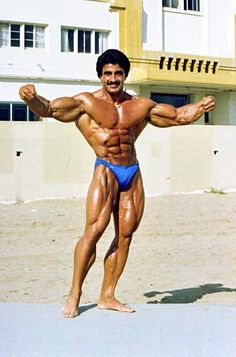 a man standing on top of a sandy beach next to a tall white building and holding his arms out