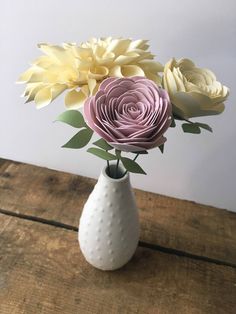 a white vase filled with flowers on top of a wooden table