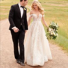 a bride and groom walking down a dirt road holding each other's hands as they look at each other