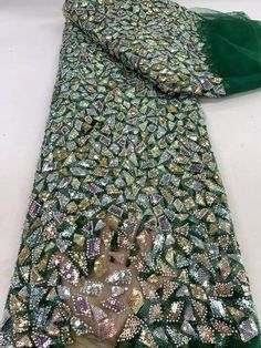 a green and gold scarf with sequins on the bottom, sitting on a white surface