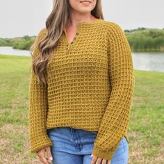 a woman standing in the grass wearing a mustard colored sweater and jeans with her hands on her hips