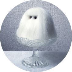 a white stuffed animal sitting on top of a glass cake plate in front of a gray background