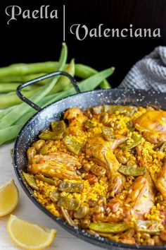 paella with chicken and green beans in a skillet next to lemon wedges