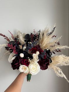 a person holding a bouquet of flowers in their left hand, with feathers on the wall behind them