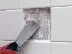 a person is using a knife to cut through the tile on a wall with white tiles