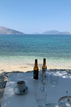 two empty beer bottles sitting on top of a white table next to the ocean and beach