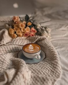 a cappuccino sits on a bed with flowers and a knitted blanket