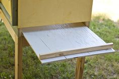 a yellow beehive sitting on top of a grass covered field next to a wooden table