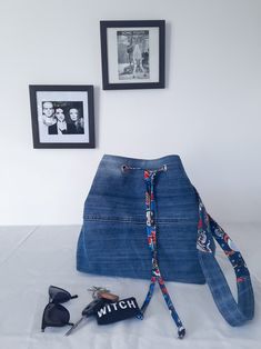 a blue jean purse sitting on top of a bed next to two framed pictures and sunglasses