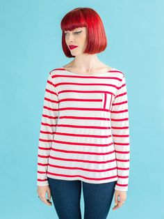 a woman with red hair wearing a white and red striped shirt standing in front of a blue background