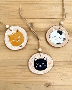 three wooden ornaments with cats on them are hanging from string and decorated with twine