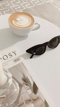 a cup of coffee sitting on top of a table next to a magazine and sunglasses