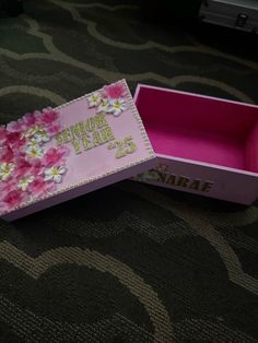 an open pink box with flowers on the inside sitting on a carpeted floor next to a wall