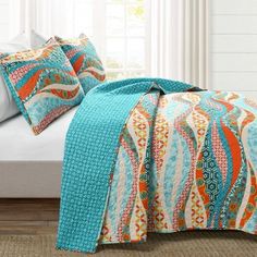 a bed covered in a blue and orange bedspread next to a white window