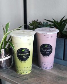 two iced drinks sitting next to each other on top of a wooden table in front of potted plants