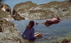 two people are swimming in the water near some rocks