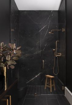 a bathroom with black marble walls and floor, along with a wooden stool in the shower