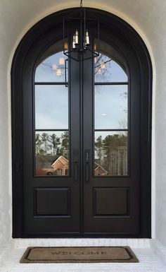 a black double door with two sidelights and a welcome mat on the front porch