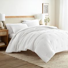 a bed with white comforter and pillows in a room next to a lamp on a table