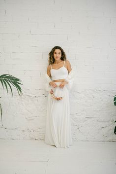 a woman standing in front of a brick wall wearing a white dress and holding a fan