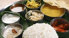 an assortment of different types of food on a leafy platter with sauces