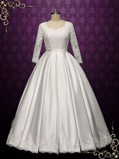 a white wedding dress with long sleeves on a mannequin head stand in front of a purple background