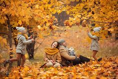 three adults and two children are sitting on the ground in front of trees with yellow leaves