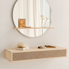 a mirror and some books on a shelf in front of a white wall with a circular mirror