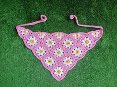 a pink crocheted bib with white and yellow daisies on it sitting on green grass