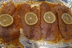 some fish with lemon slices on top of it sitting on tin foil and ready to be cooked