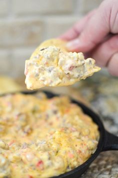 a hand holding a spoon full of food over a skillet filled with eggs and cheese