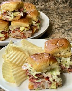 two plates filled with sandwiches and chips on top of a marble countertop next to each other