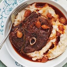 a white plate topped with meat and mashed potatoes covered in gravy next to a fork