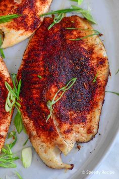 two pieces of chicken on a white plate with green garnish and seasoning