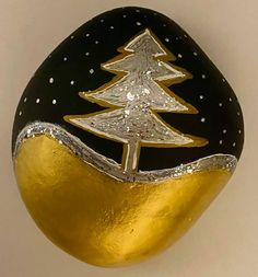 a black and gold painted rock with a christmas tree on it's side, against a white background