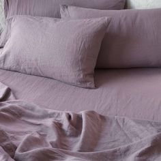 an unmade bed with purple sheets and pillows