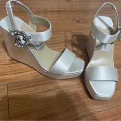 Brand New - Only Worn Once For About 3 Hours. With Original Box And Dust Bag, White Satin Jimmy Choo Wedges With A Crystal Embellished Buckle. Perfect For A Bride/Wedding. Very Comfortable - Size 38.5 (Size 8 In Us) Elegant High Heel Wedge Sandals With Branded Heel, Elegant Wedge Sandals With Heel Strap, Chic Ankle Strap Wedge Sandals For Wedding, Designer Wedding Platform Heels, Elegant Formal Wedge Sandals With Removable Insole, Elegant Wedge Sandals With 4-inch Heel, Luxury White Platform Wedge Sandals, Elegant Formal Wedge Sandals With 4-inch Heel, Chic White Wedge Sandals For Formal Occasions