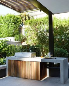 an outdoor kitchen with a grill on the counter and trees in the backgroud