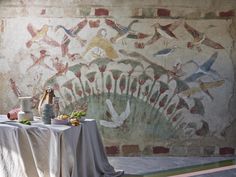 a table with food and vases on it in front of a painted wall mural