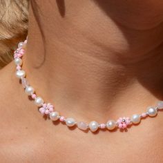 a woman wearing a pink and white necklace with pearls on it's collarline