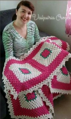 a woman sitting on a couch holding a pink and white crocheted blanket