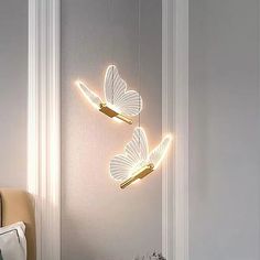 two white butterflies hanging from the side of a wall next to a bed and nightstand