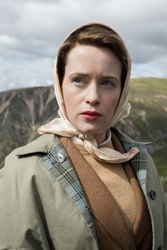 a woman with a scarf on her head standing in front of a mountain and cloudy sky