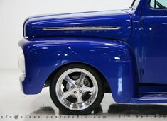 an old blue truck with chrome rims on it's tires is parked in a white room