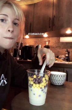 a woman sitting at a table in front of a glass filled with cereal and milk