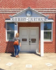 a woman standing in front of a building with a clock on it's side