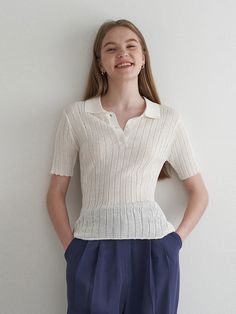 a woman standing in front of a white wall with her hands on her hips and smiling