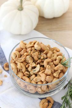 a glass bowl filled with cashews on top of a white napkin next to pumpkins