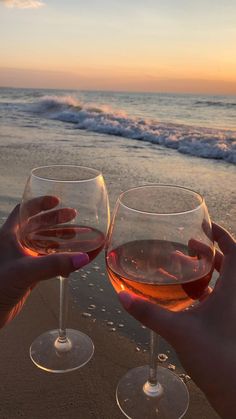 two people toasting wine glasses on the beach at sunset with waves in the background