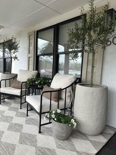 two white chairs sitting on top of a checkered floor next to plants and windows